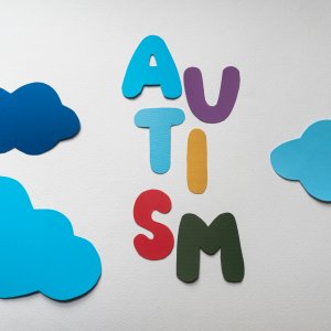 Vibrant letters spelling 'AUTISM' surrounded by blue paper clouds on a white background.
